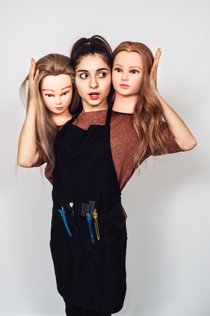 Young girl hairdresser holds in hands two mannequin heads