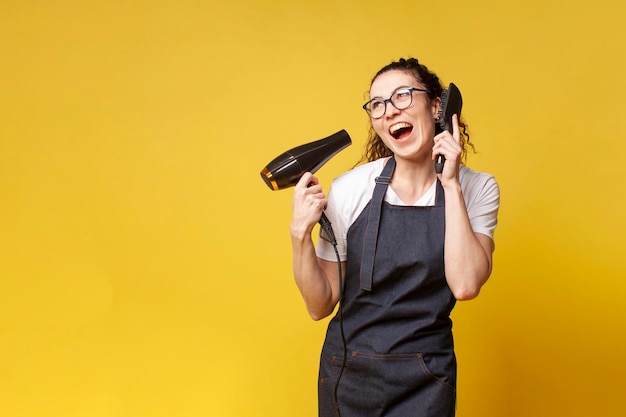 Young girl hairdresser in uniform holds a hair dryer and imitates a conversation on the phone