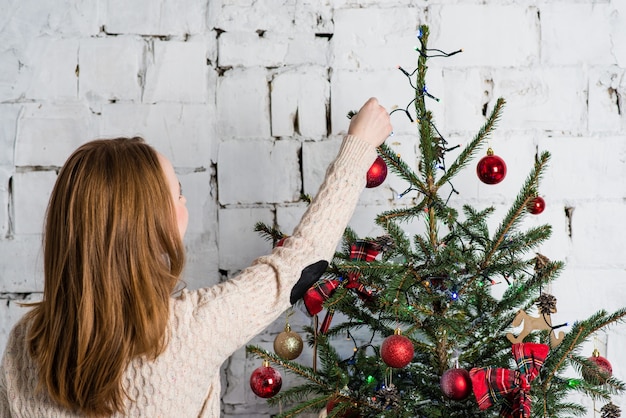 クリスマスツリーに赤いボールをぶら下げている少女。クリスマスと新年のコンセプト。