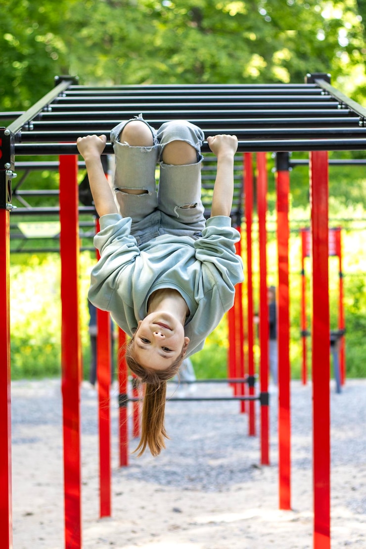 Photo young girl hanging upside down on a jungle gym in outdoor park