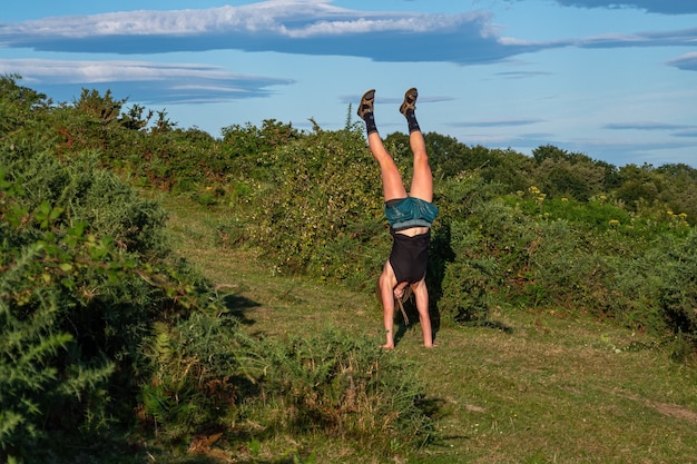 Young girl in a hat doing a handstand on the green hill