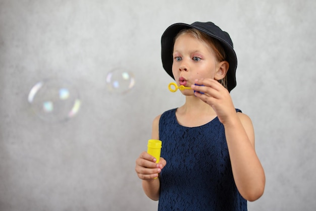 Young girl in a hat and dress blows bubbles