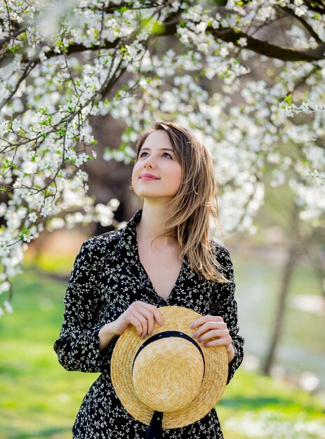 Young girl in a hat stay near a flowering tree 