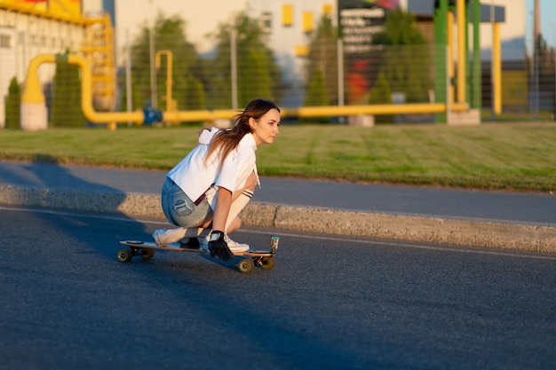 道路上のスケートボードを楽しんで若い女の子。晴れた日にスケートの若い女性