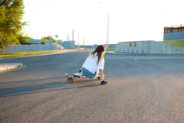 Молодая девушка весело с скейтборд на дороге. Молодая женщина катается на коньках в солнечный день