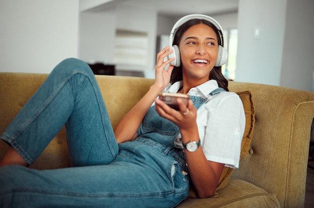 Young girl headphones and music with smartphone relax at home with technology and listening to podcast radio and audio streaming Online social network and happy on sofa with sound and wellness