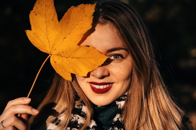 Young girl hides her face with yellow maple leaves