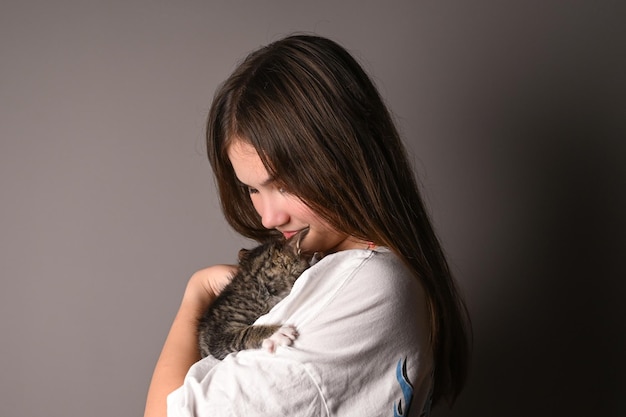 Young girl holding a baby cat on gray background Female hugging her cute kitty Adorable domestic pet concept