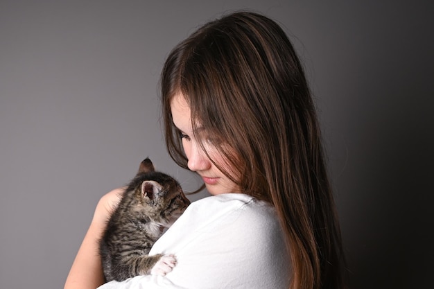 Young girl holding a baby cat on gray background Female hugging her cute kitty Adorable domestic pet concept