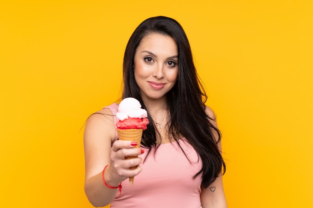 Ragazza che tiene un gelato della cornetta sopra la parete gialla con l'espressione felice