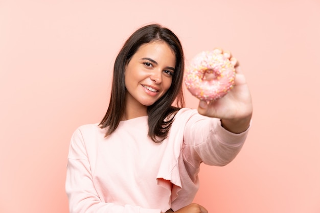 Young girl holding a donut over isolated pink wall