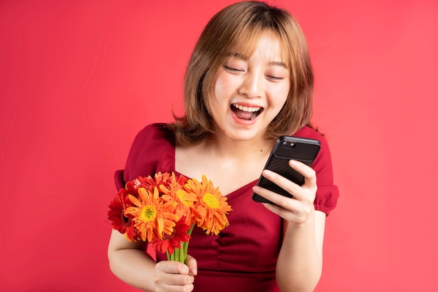 Young girl holding flowers and using phone with cheerful expression on pink