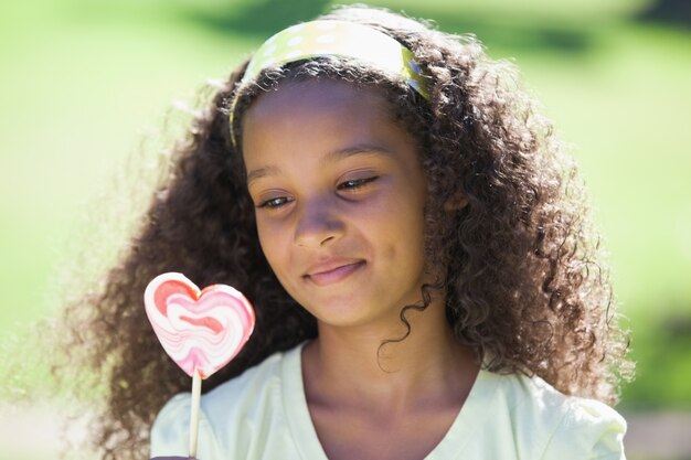 Ragazza che tiene una lecca-lecca del cuore nel parco