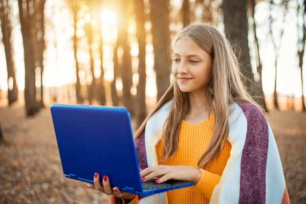 Young girl holding laptop in hands, standing in bright autumn park