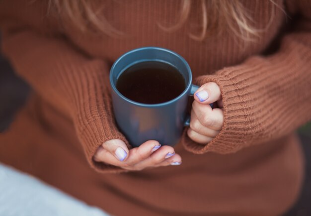 手でホットコーヒーのマグカップを保持している若い女の子