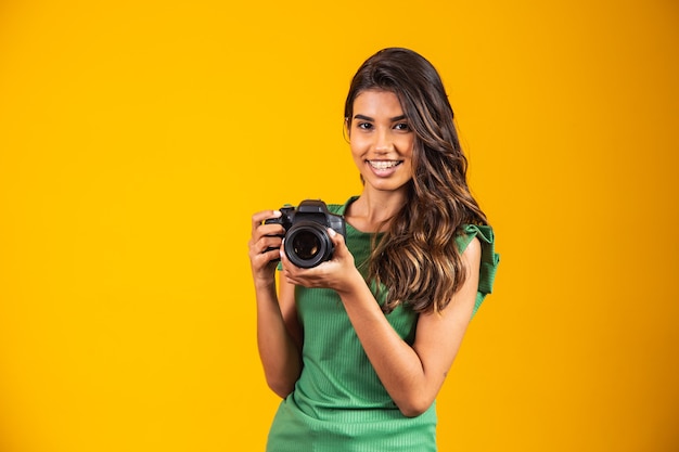 Young girl holding a photo camera on yellow background. woman taking picture