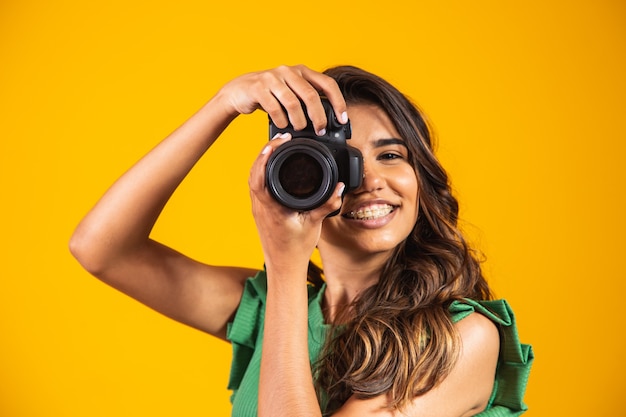 Young girl holding a photo camera on yellow background. woman taking picture