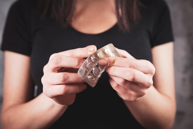 Young girl holding pills in hand on gray background