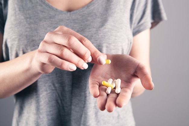 Young girl holding pills in hand on gray