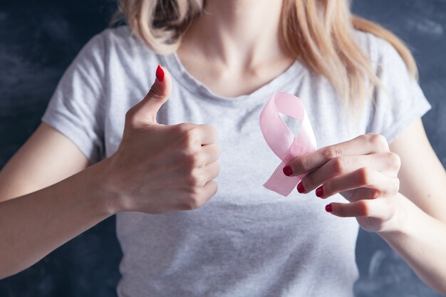 Young girl holding a pink ribbon and showing thumb up