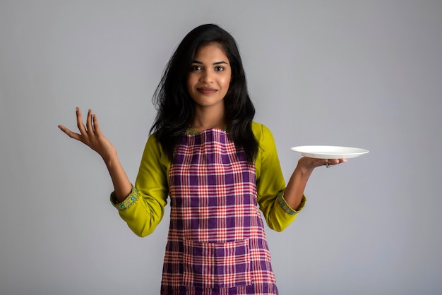 Молодая девушка держит и позирует с кухонной утварью, тарелкой и миской на сером