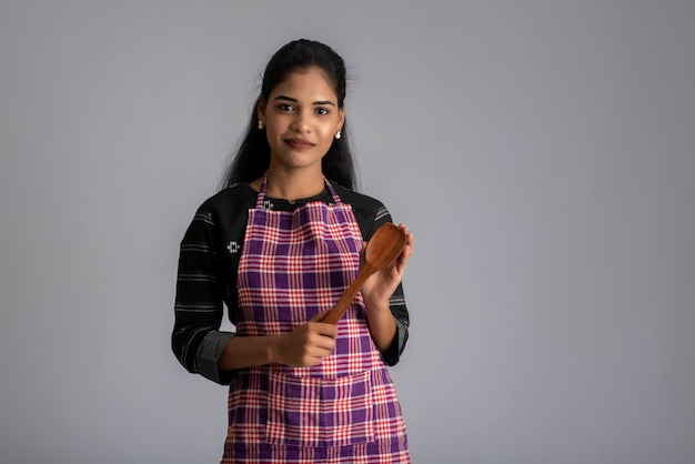 Young girl holding and posing with kitchen utensils spatula on a grey wall