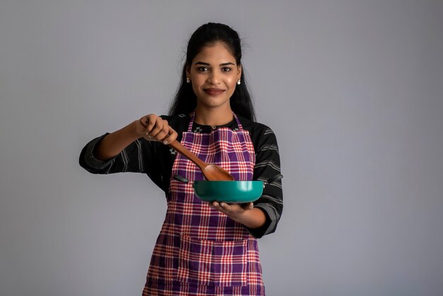 Young girl holding and posing with kitchen utensils spatula and pan on a grey wall