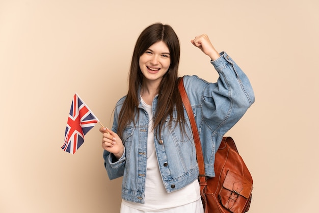 Young girl holding an United Kingdom flag isolated on beige celebrating a victory