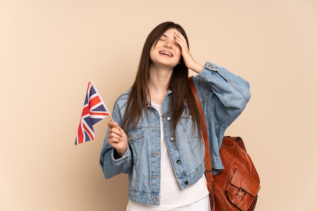 Young girl holding an United Kingdom flag isolated on beige smiling a lot