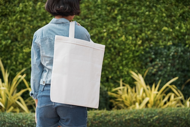 Молодая девушка держит белую сумку из ткани в парке