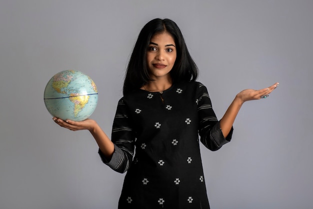 Young girl holding the world globe and posing on grey.