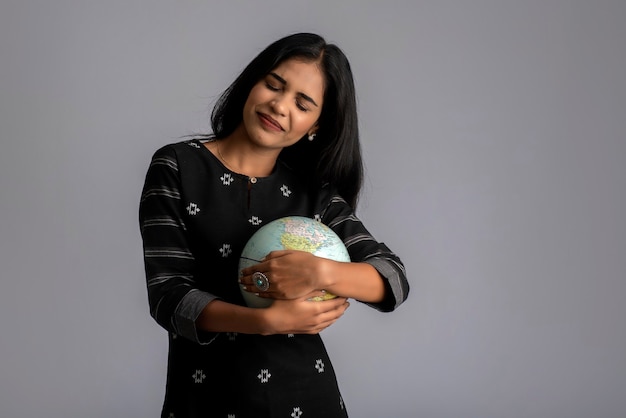 Young girl holding the world globe and posing on grey.