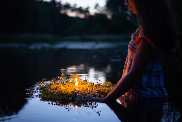 Young girl holding wreath with burning candle setting it to flow on the river making a wish