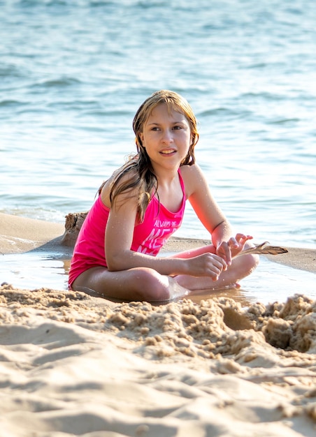 Photo young girl holds a bird feather as she decorates a sand castle on the beach