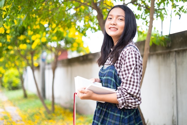 A young girl holds a book and standing under a beautiful tree