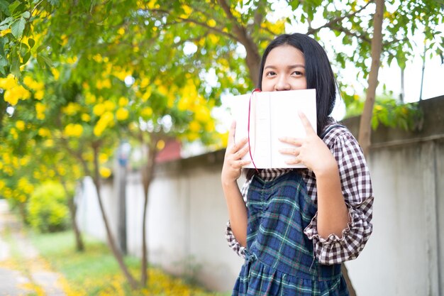 A young girl holds a book and standing under a beautiful tree