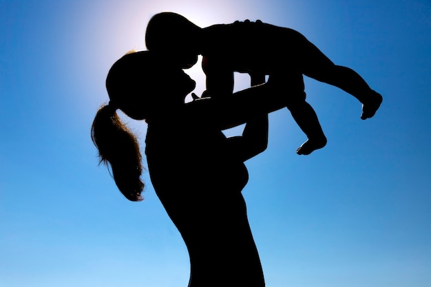 A young girl holds a child in her arms against the sun. Silhouette photography. High quality photo