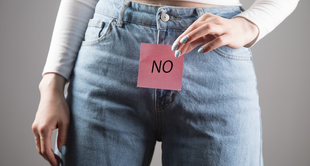 Young girl holds the inscription "NO" between her legs on a gray scene