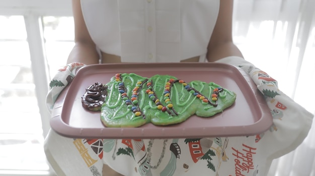 Young girl holds large Christmas pine tree cookie with chocolates ornaments on tray