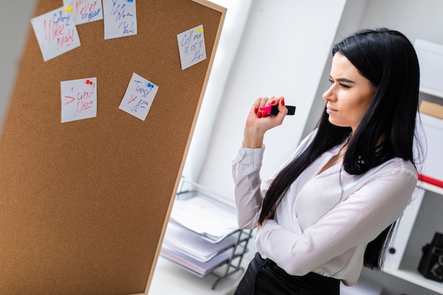 A young girl holds a marker in her hand and stands near the board with stickers.