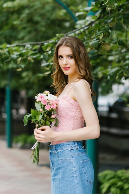 A young girl holds pink roses in her hands while walking in the summer in the Park