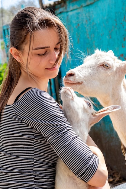 A young girl holds a small goat near the goat, the girl takes care of the goats