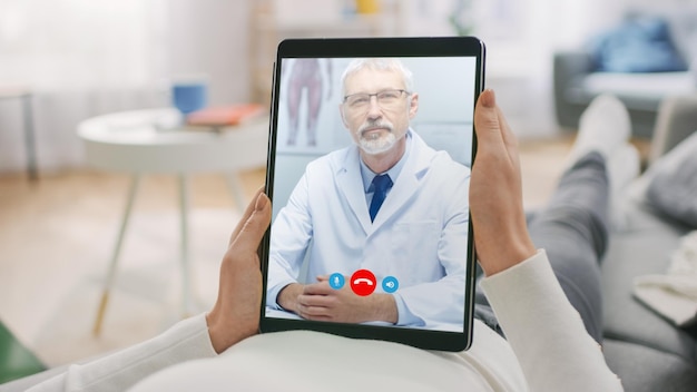 Foto ragazza a casa che usa il tablet digitale per parlare con il suo medico tramite app medica di videoconferenza donna controlla i possibili sintomi con un medico professionista usando un'applicazione di video chat online