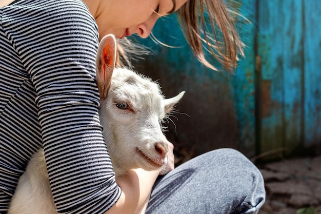 Молодая девушка обнимает молодую белую козу, любит животных