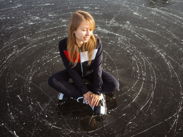 Молодая девушка на коньках сидит на льду озера