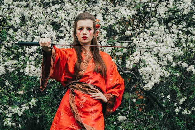 Фото Молодая девушка в традиционном кимано в цветущем саду с самурайским японским мечом катана в образе женщины-воина