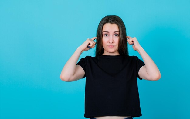 Young girl is closing ears with fingers on blue background