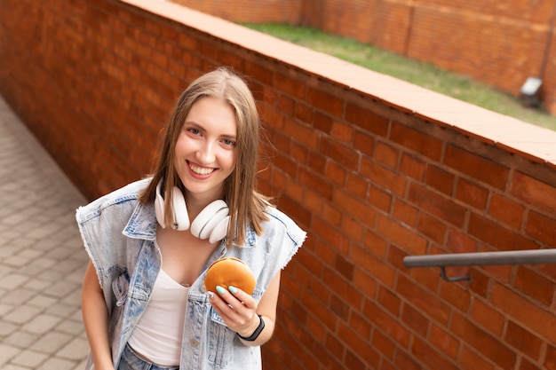 Photo a young girl is eating her burger right on the street. she has fun enjoying a delicious snack.