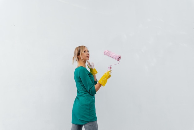 A young girl is engaged in repairs and paints a white wall with a roller in a new apartment Renovation of the interior and a new apartment Housewarming and a desirable mortgage