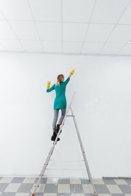 A young girl is engaged in repairs on the stairs and paints a\
white wall with a roller in a new apartment renovation of the\
interior and a new apartment housewarming and a desirable\
mortgage